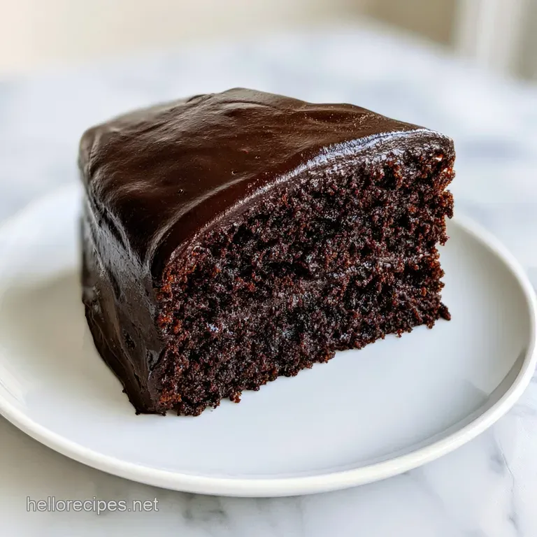 A tall, dark chocolate cake on a white marble pedestal, topped with a mirror-like glaze and a single mint leaf.